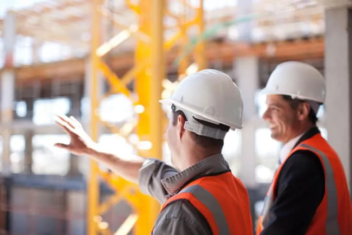 Two men with hard hats pointing and talking.