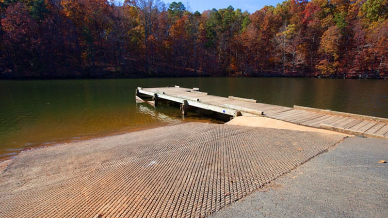 Boat ramp on lake with autumn trees in the distance.